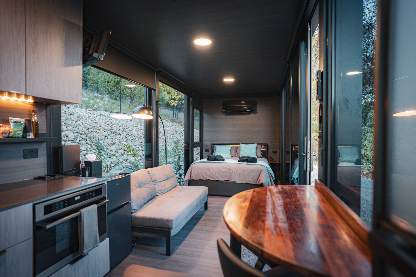 Tiny home bedroom with bed, sofa, and kitchen area in a compact living space.