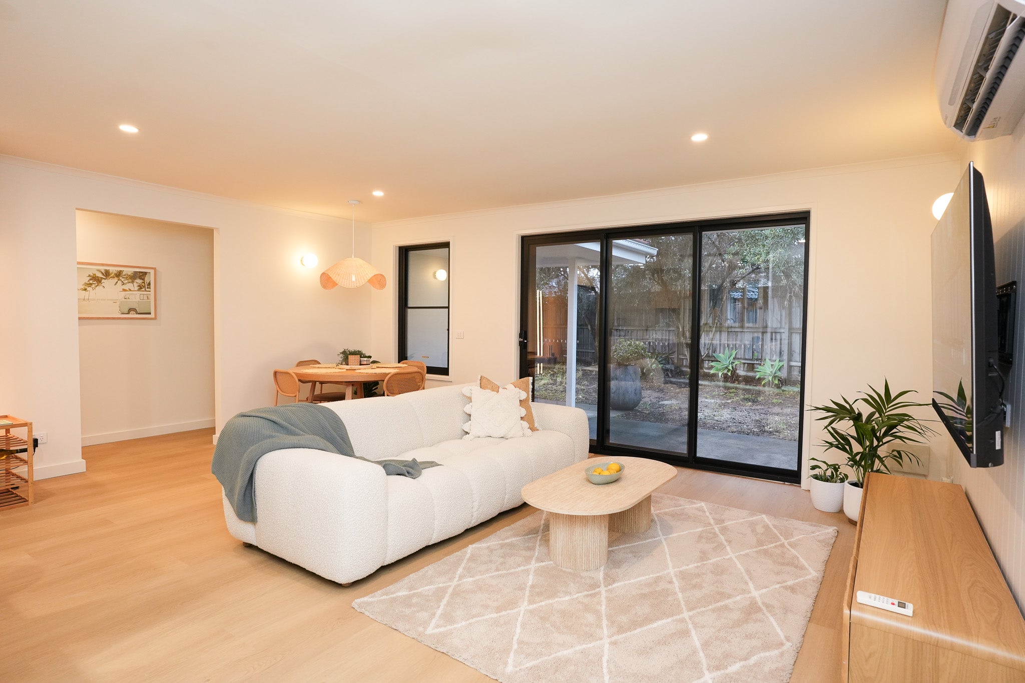Bright living area of the Capel Sound accommodation with a plush white sofa, dining nook, and sliding doors leading to the garden.