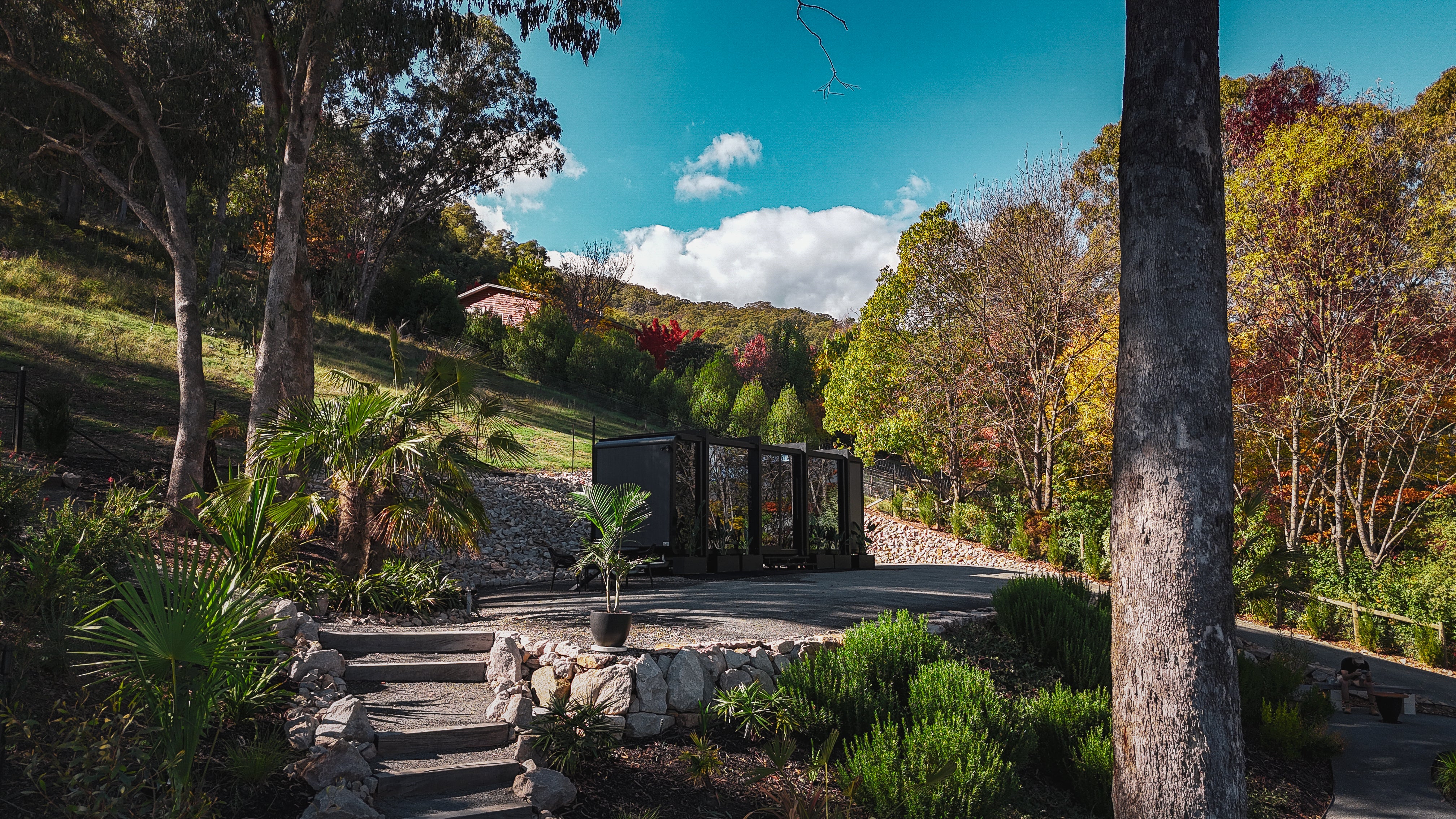 Exterior view of the 8m Bright Elsewhere Pod nestled in the hills of Victoria, surrounded by lush greenery and autumn colours.