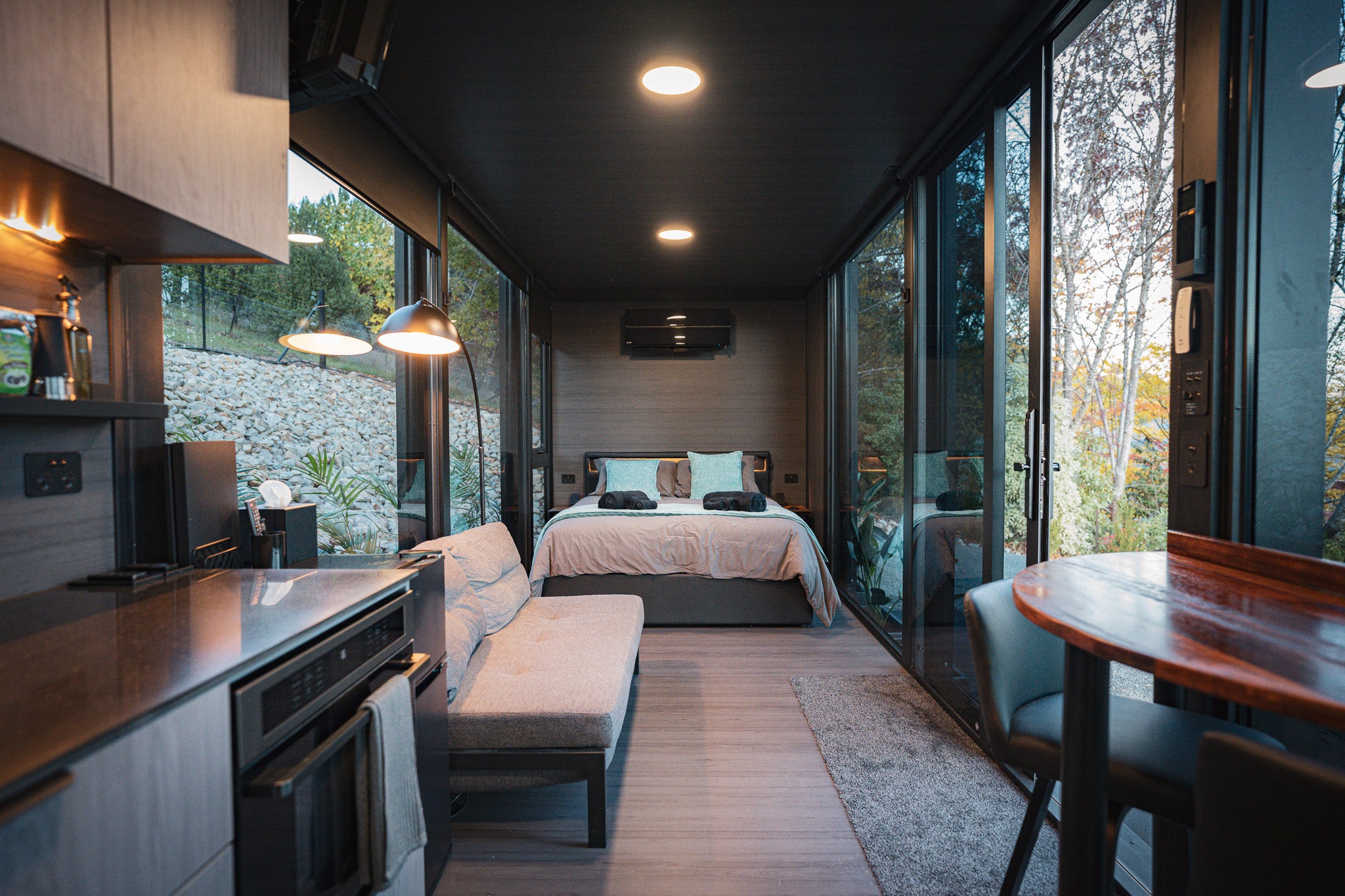 Interior of the 8m Bright Elsewhere Pod featuring a queen bed, lounge and large glass windows overlooking the Bright alpine landscape in Victoria.