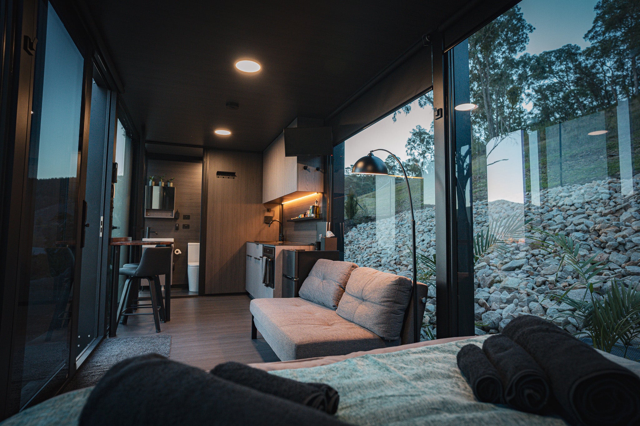 Inside the Bright Elsewhere Pod showing a compact lounge area, kitchenette, and panoramic windows overlooking the Victorian hillside.