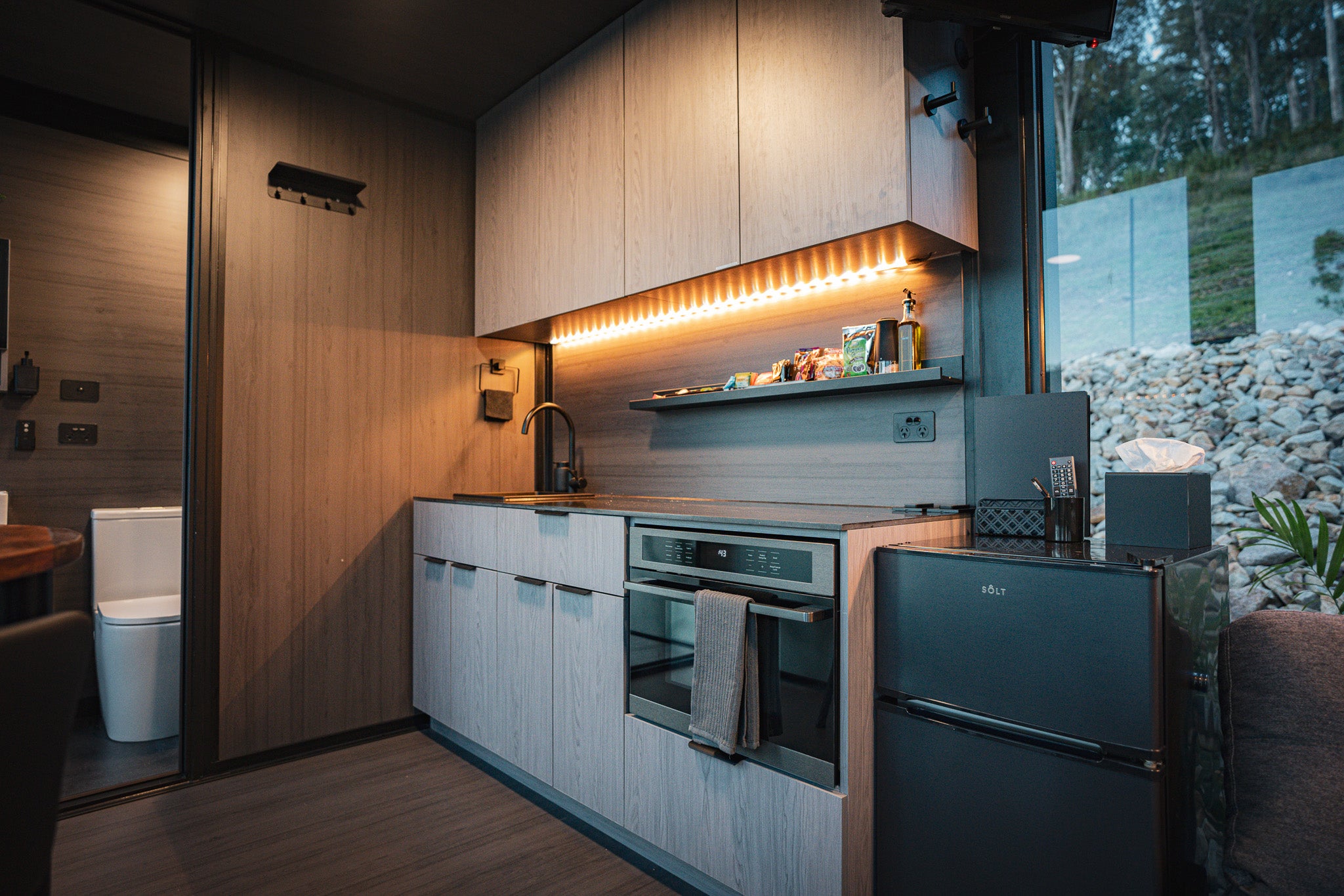 Kitchenette inside the Bright Elsewhere Pod with wood cabinetry, modern appliances, and ambient lighting for a warm, inviting feel.