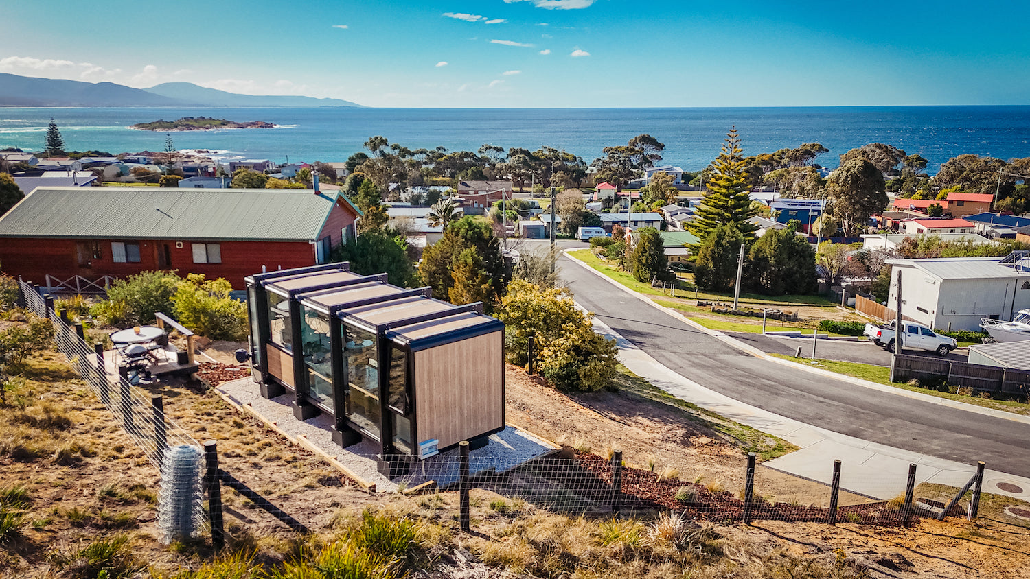 An aerial video of a luxury modular pod set up for use as an airbnb. The pod is a beautiful glass structure overlooking an ocean vista.